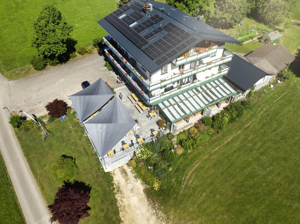 Luftaufnahme des Seegasthof Anneliese mit zwei freistehenden Doppeldreieck-Sonnensegeln über dem Gastgarten, aufgenommen aus der Vogelperspektive.