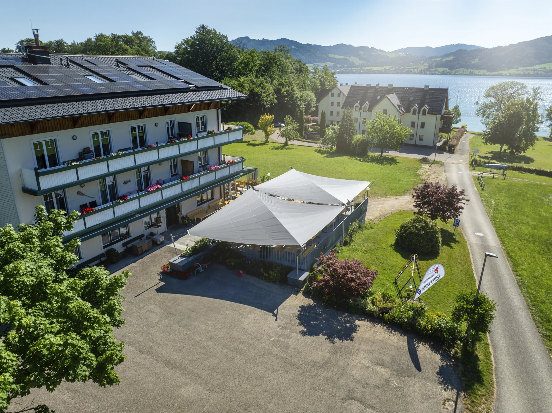 Drohnenaufnahme von zwei Doppel-Dreieck Sonnensegel als Gastro Sonnenschutz freistehend im Gastgarten den Betrieb Seegasthof Anneliese am Attersee sieht man seitlich