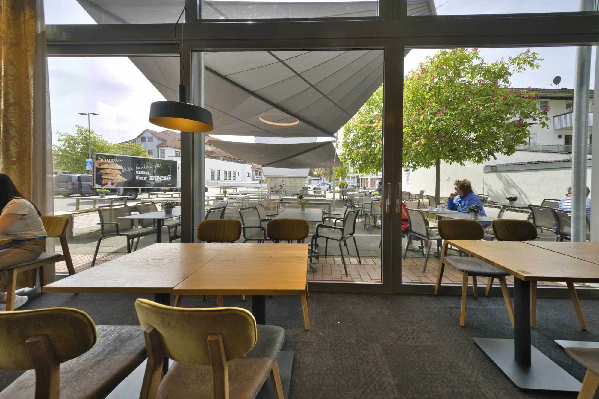 Blick aus dem Innenraum von Backhaus Häussler durch die Glasfront auf die beschattete Terrasse