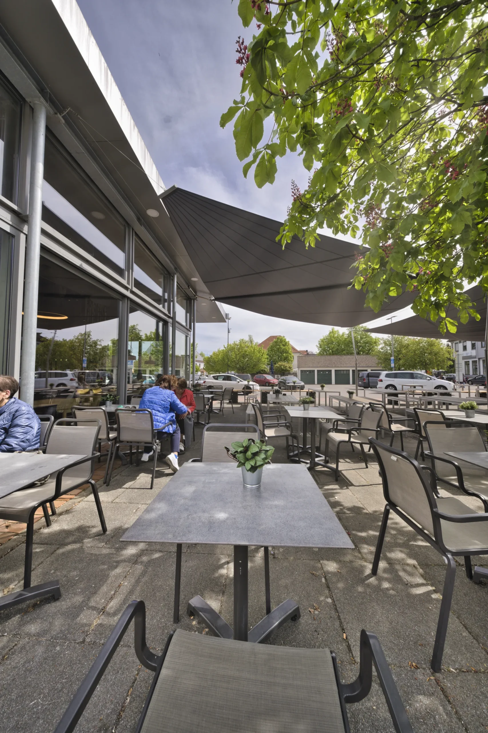Gäste auf der Terrasse von Backhaus Häussler unter Kastanie und Sonnensegel in Illertissen