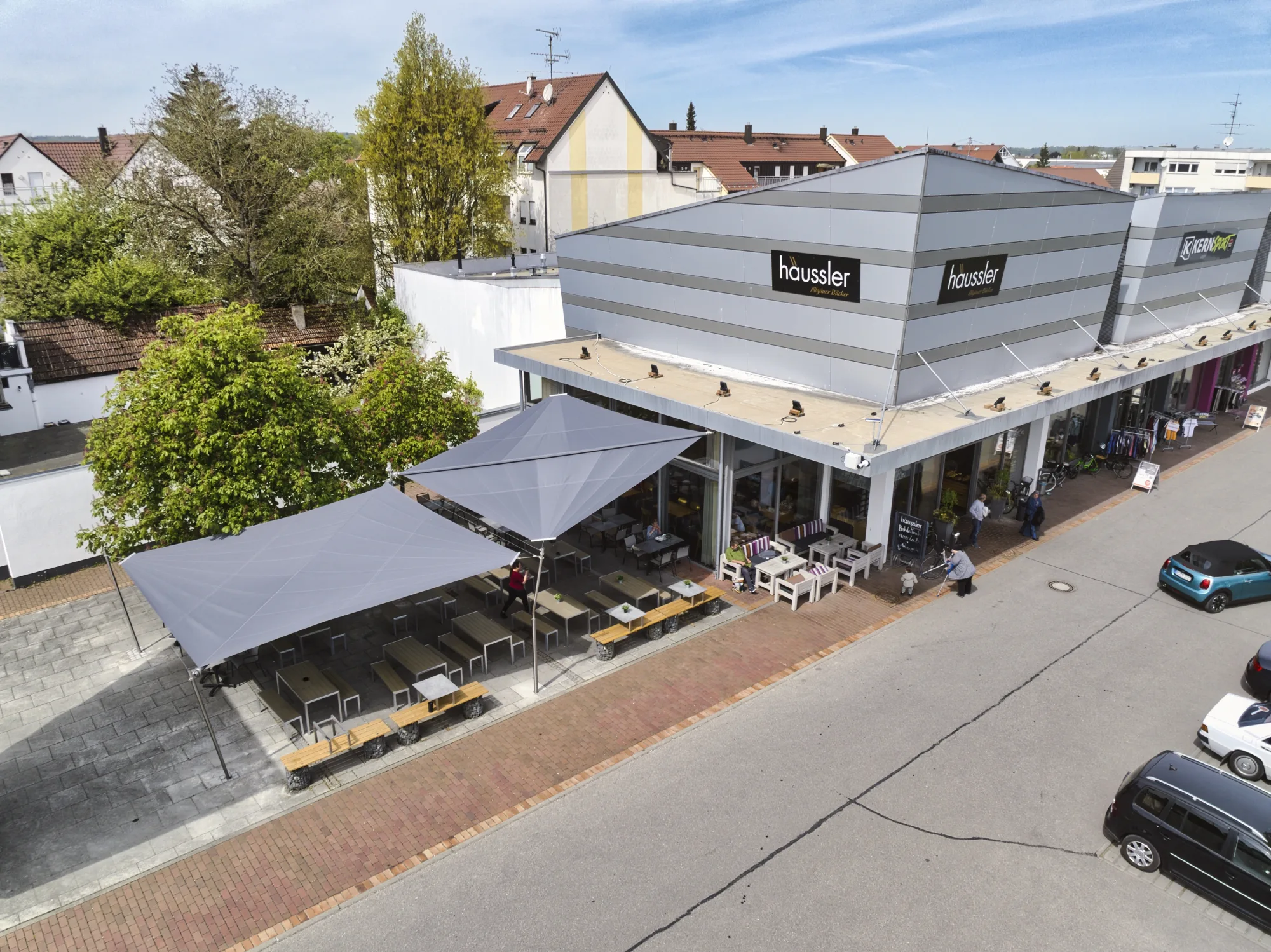 Seitliche Luftaufnahme der Filiale von Backhaus Häussler mit Sonnensegel über der Café-Terrasse in Illertissen