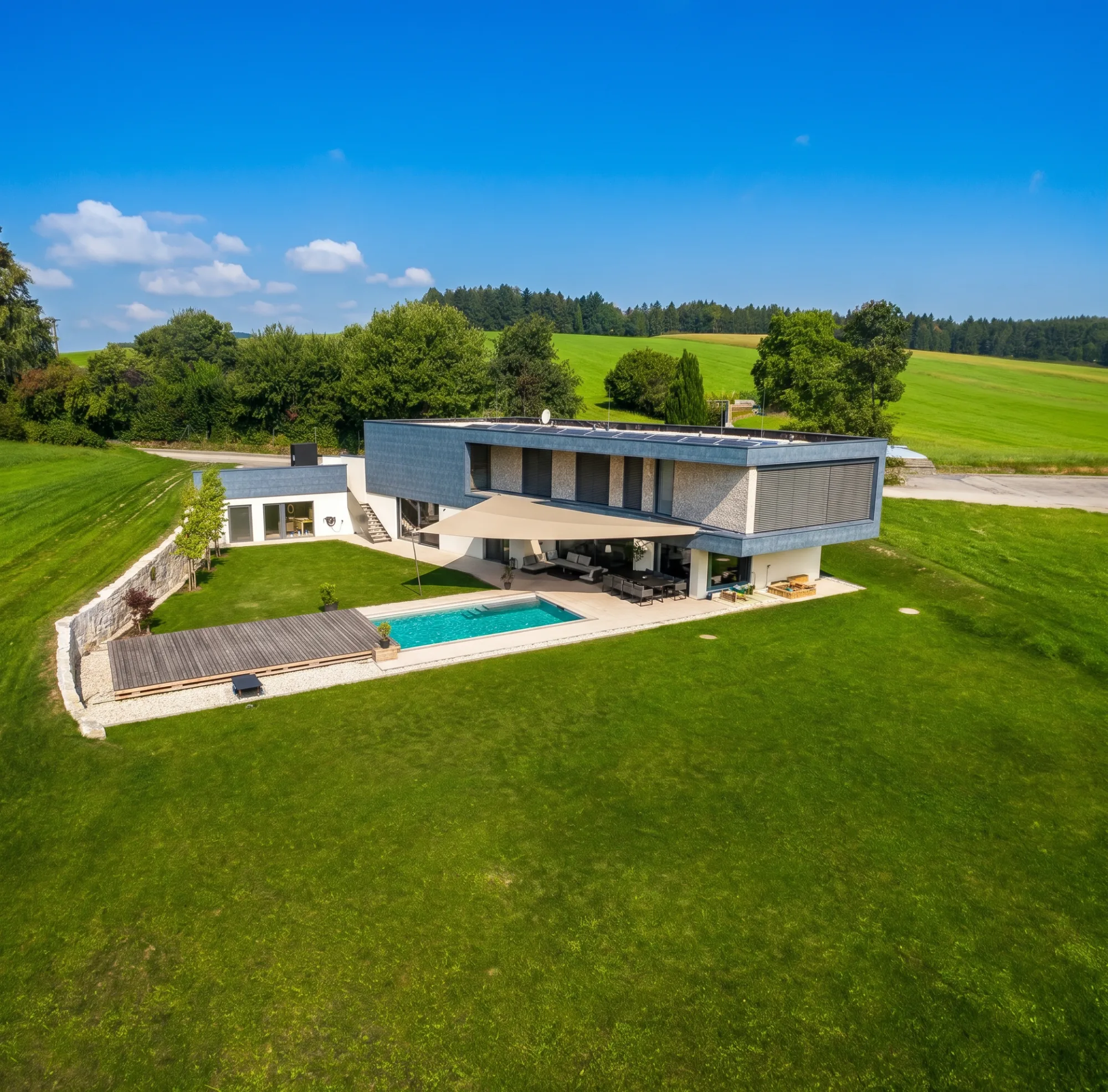 Modernes Landhaus mit Sonnensegel über Pool und Terrasse an einem strahlenden Sommertag, Luftaufnahme