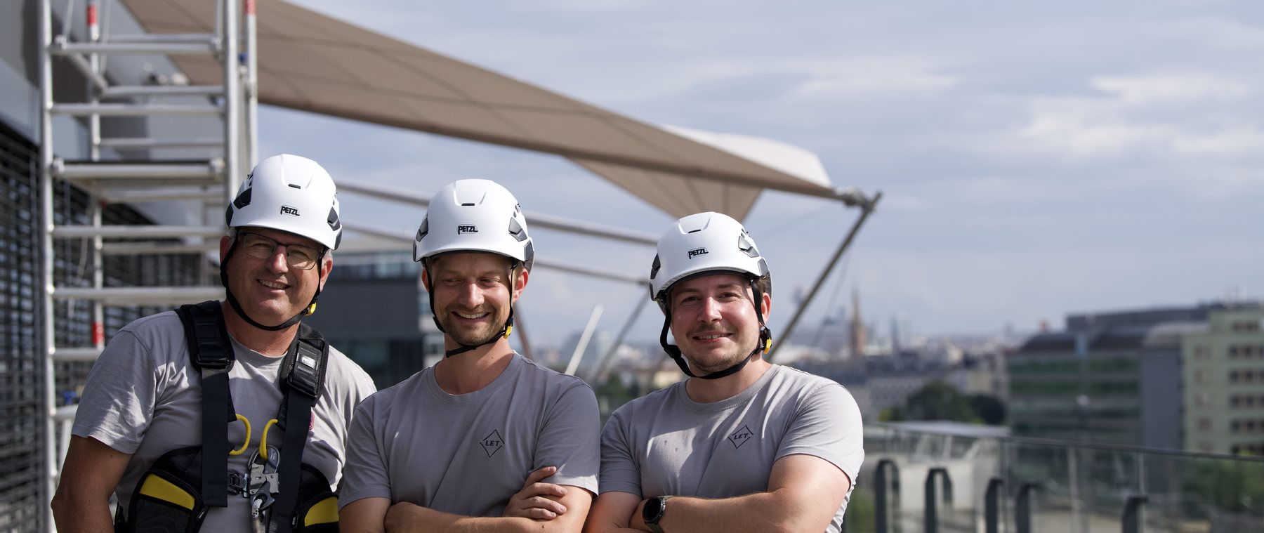 Drei LET-Monteure mit Helmen vor dem montierten Sonnensegel auf einer Dachterrasse in Wien