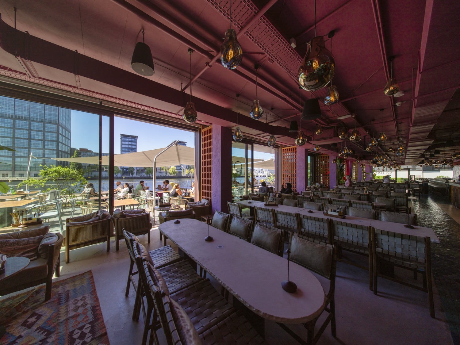 Blick aus dem Innenraum durch die offene Glasfront auf die beschattete Spree-Terrasse des Of Eden in Berlin
